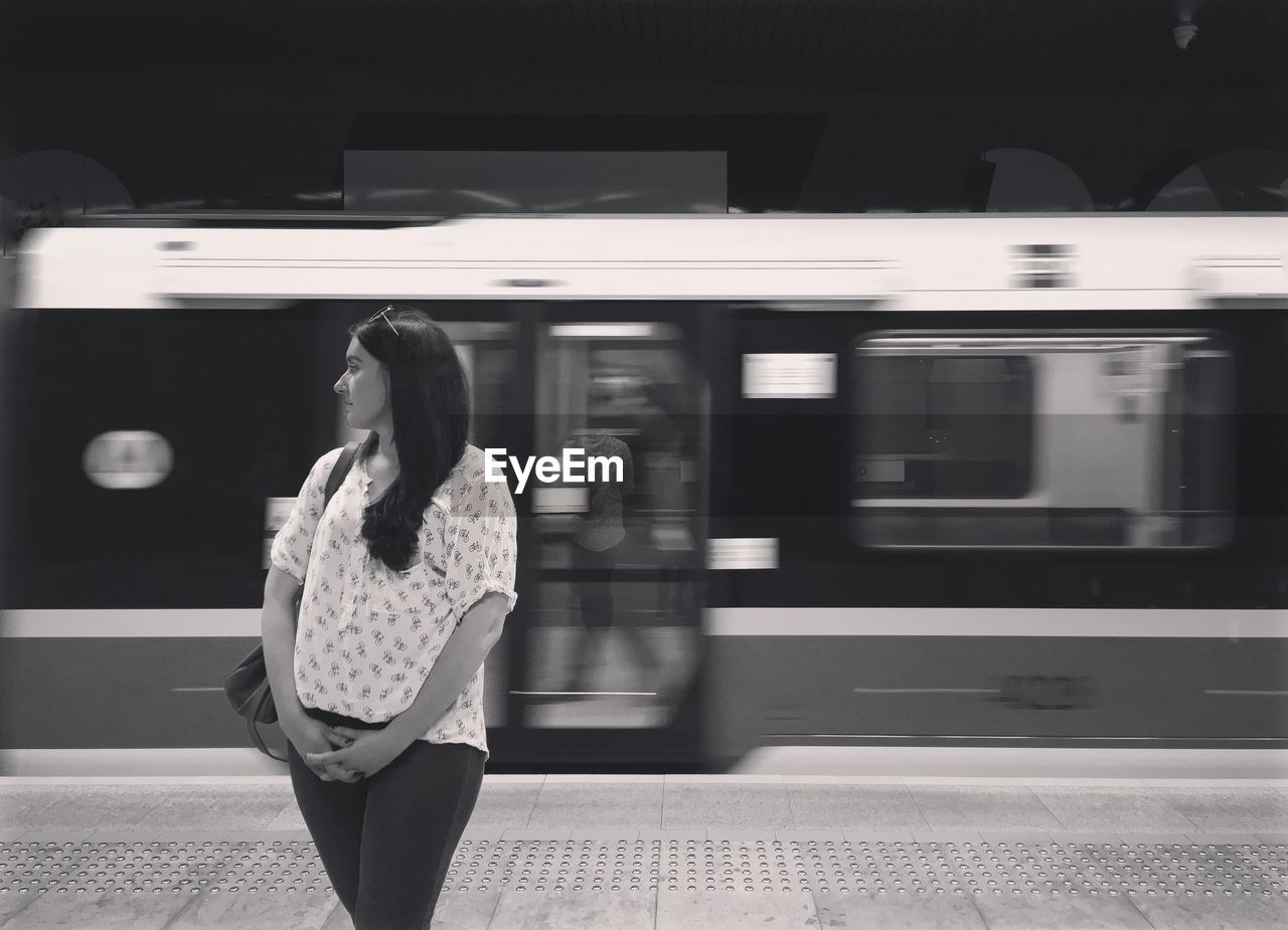 Woman standing against blurred train moving at station