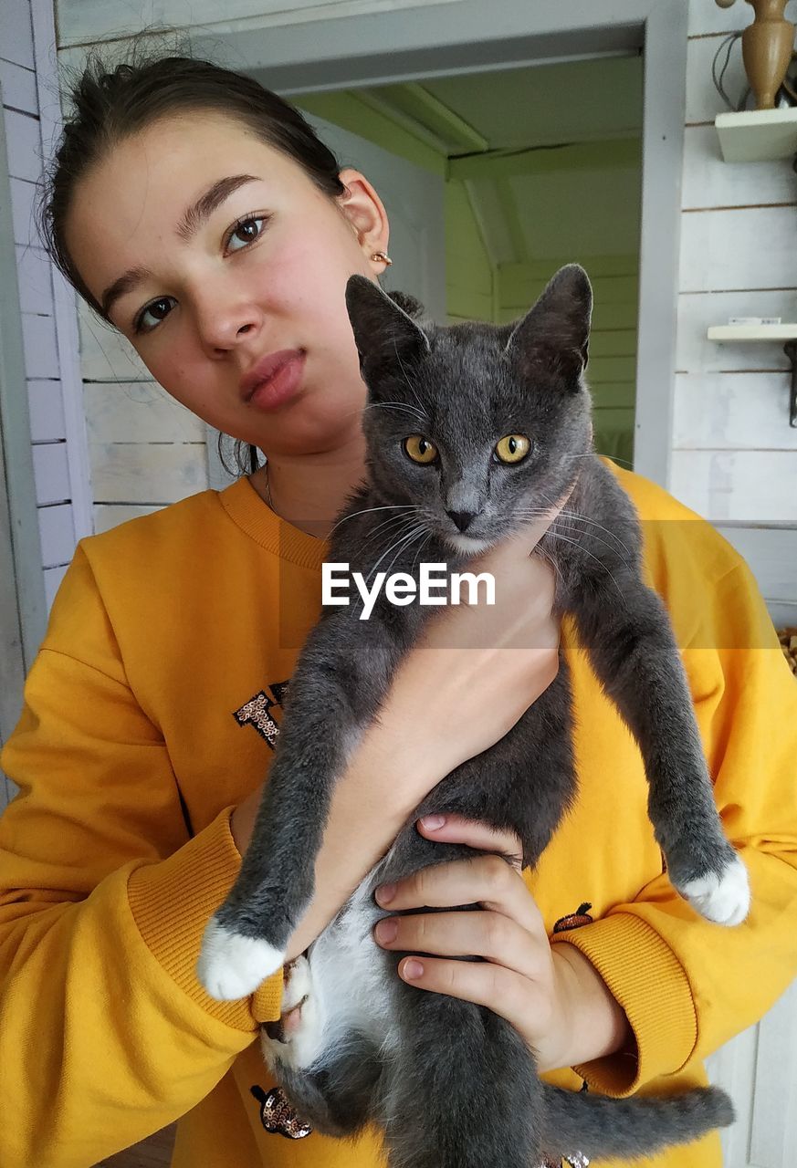 Portrait of girl holding cat while standing at home