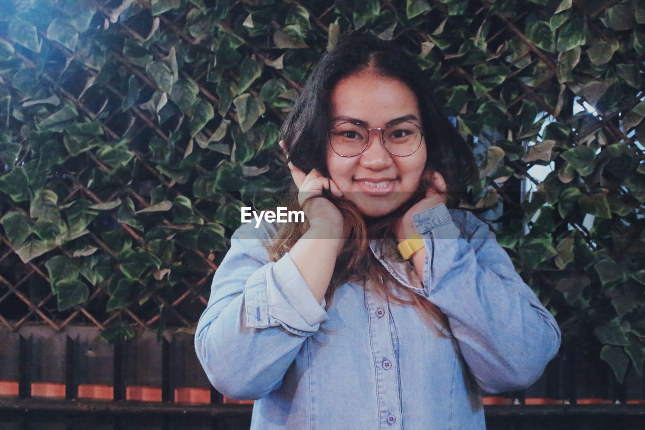 Portrait of woman covering ears while standing against plants