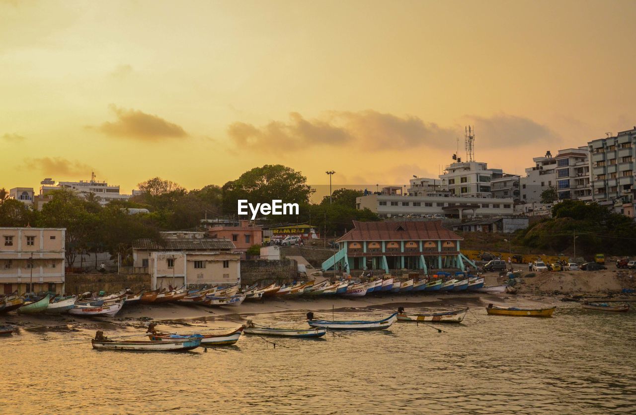 BOATS MOORED AT HARBOR BY TOWN AGAINST SKY