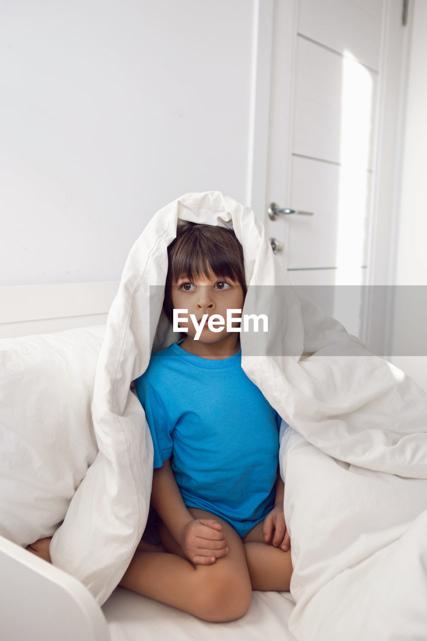 Child boy lies in a white children's bed with a blanket in a room