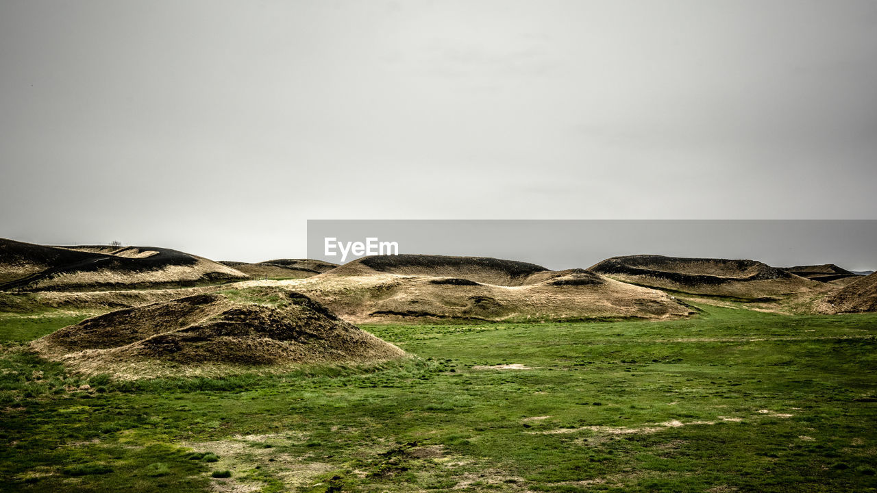 Idyllic shot of rock formation on green landscape against sky