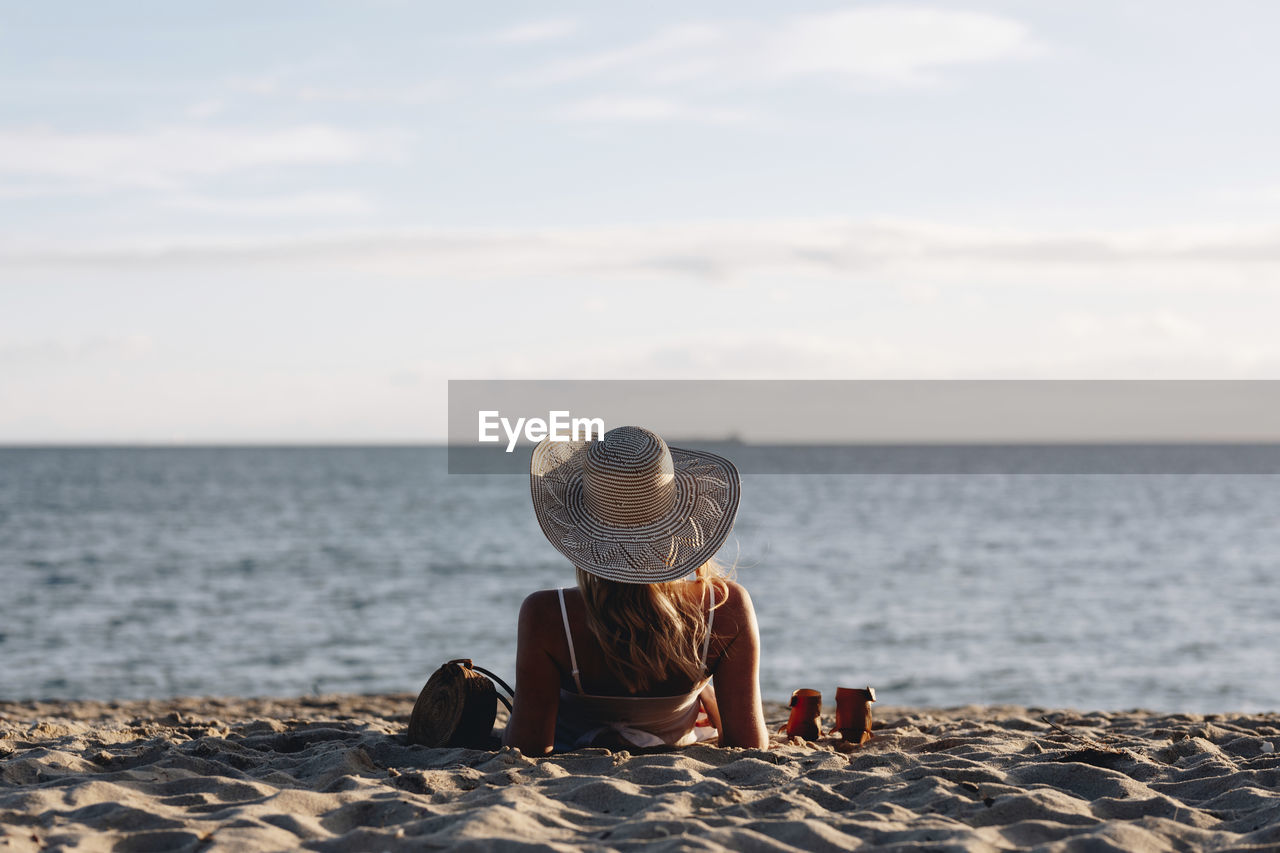 Rear view of woman wearing hat lying at beach against sky