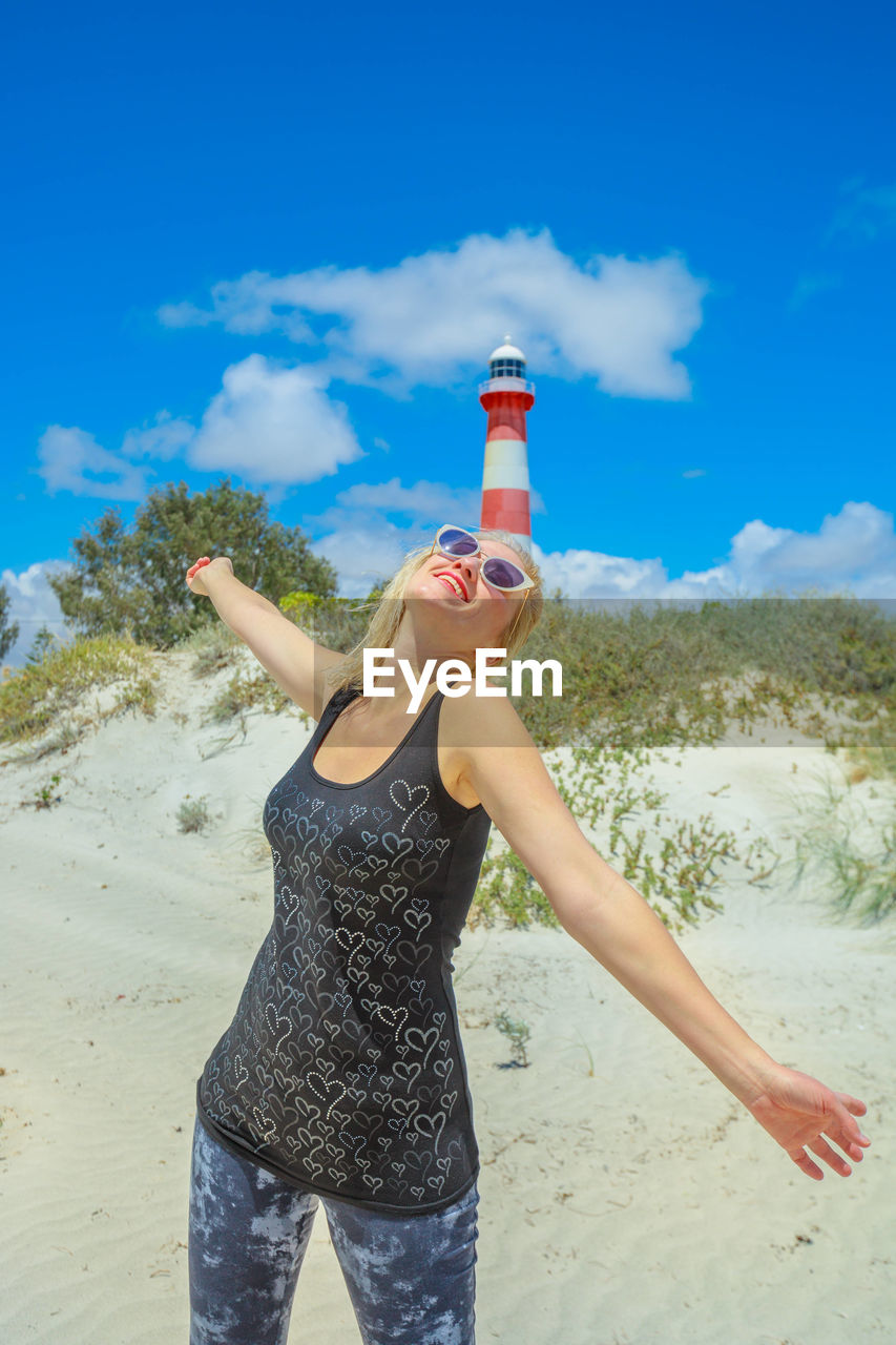 Woman with arms outstretched standing against lighthouse