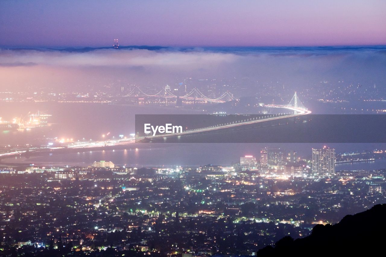 Aerial view of illuminated bay bridge and cityscape at night