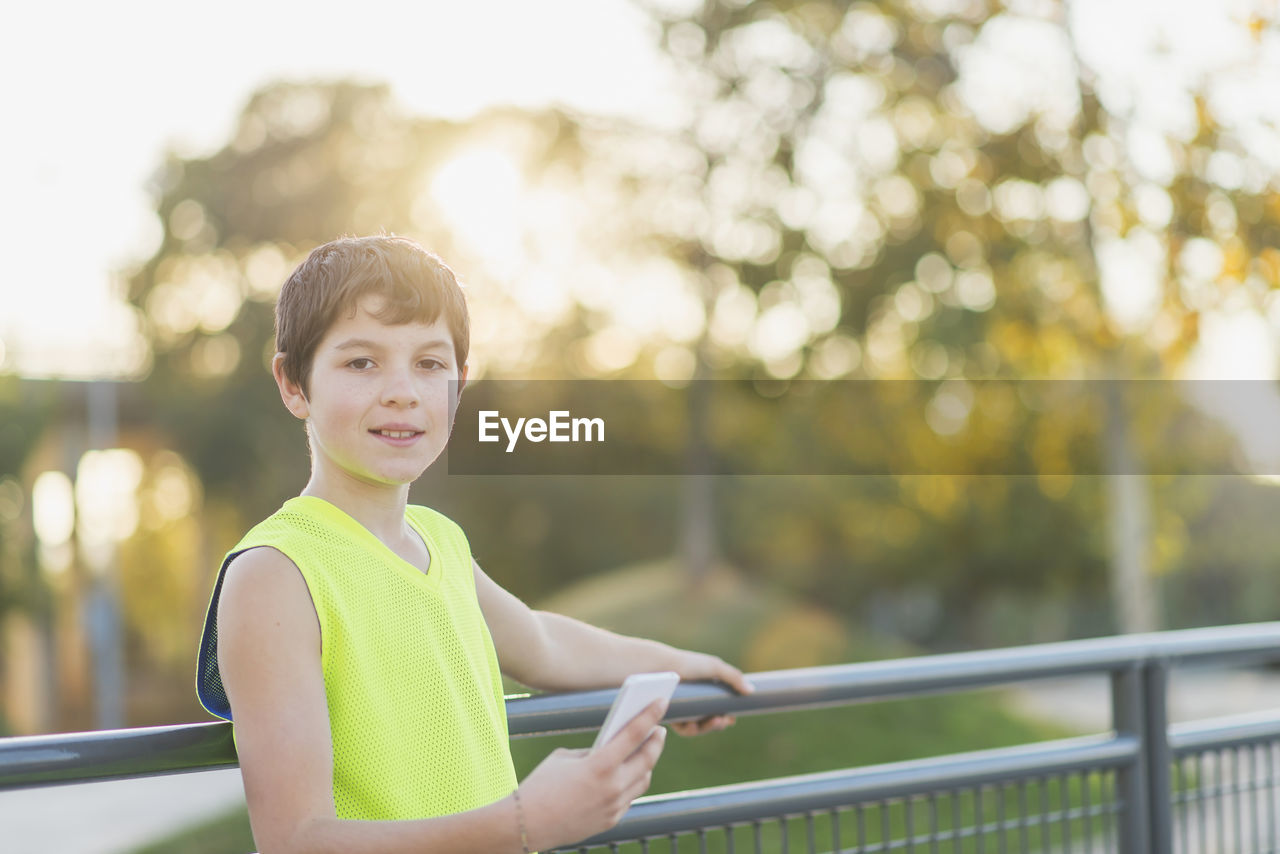 Portrait of boy using mobile phone while standing against trees