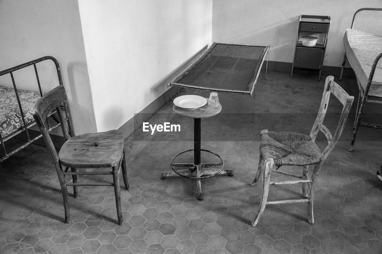 EMPTY CHAIRS AND TABLE AGAINST WALL IN ABANDONED BUILDING