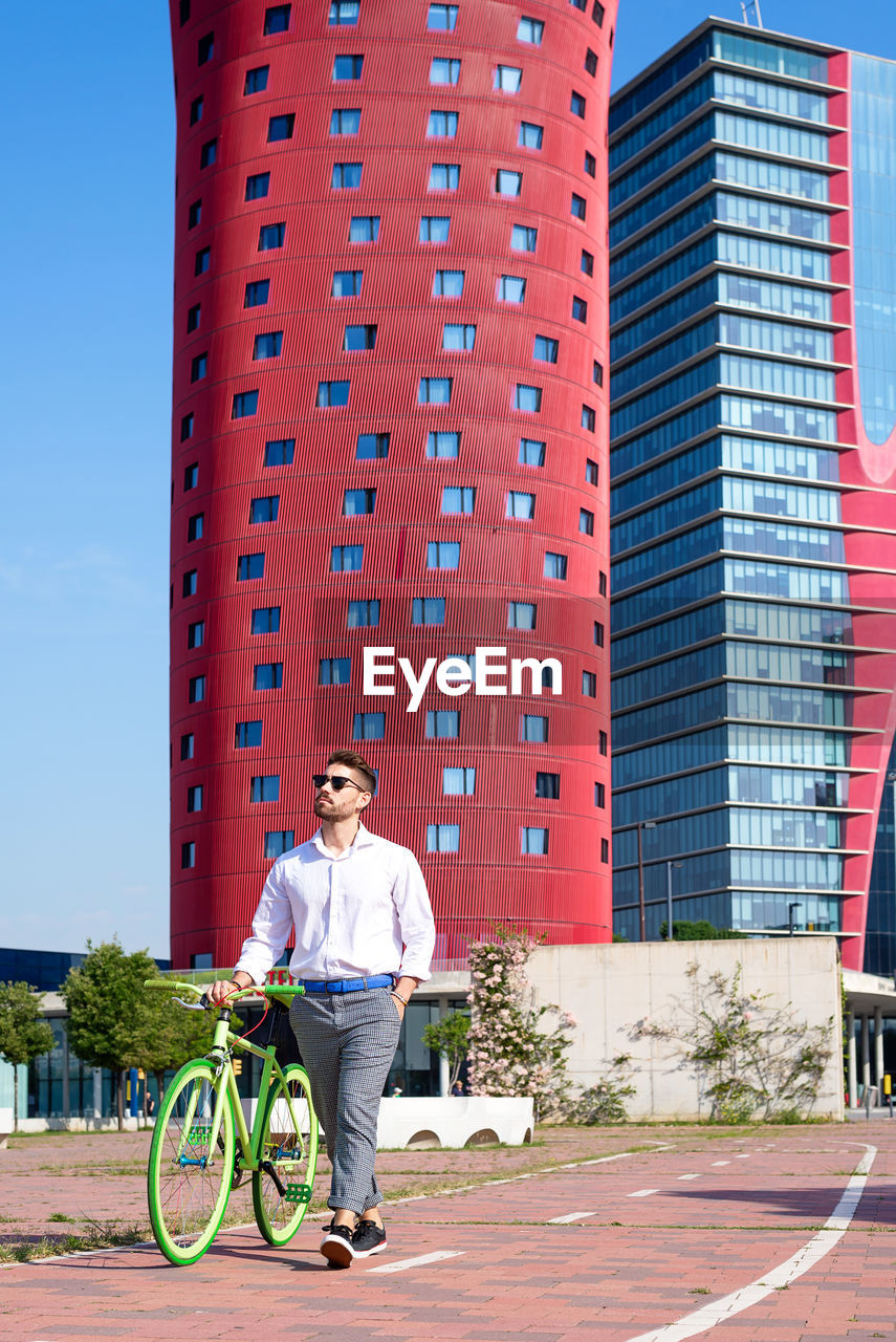 Bearded man in sunglasses walking with bike by bicycle track outdoors