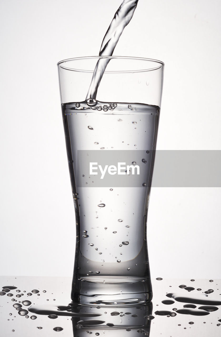 Close-up of water pouring in drinking glass against white background