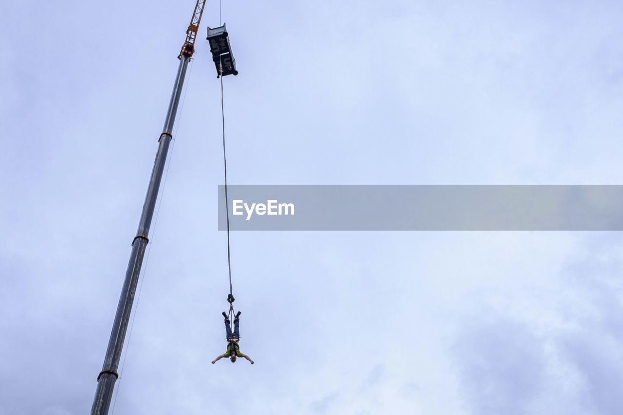 Low angle view of man bungee jumping from crane against sky