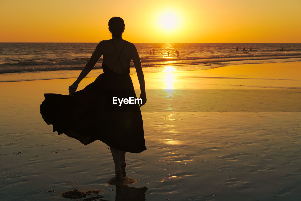 Silhouette woman walking at beach against clear orange sky