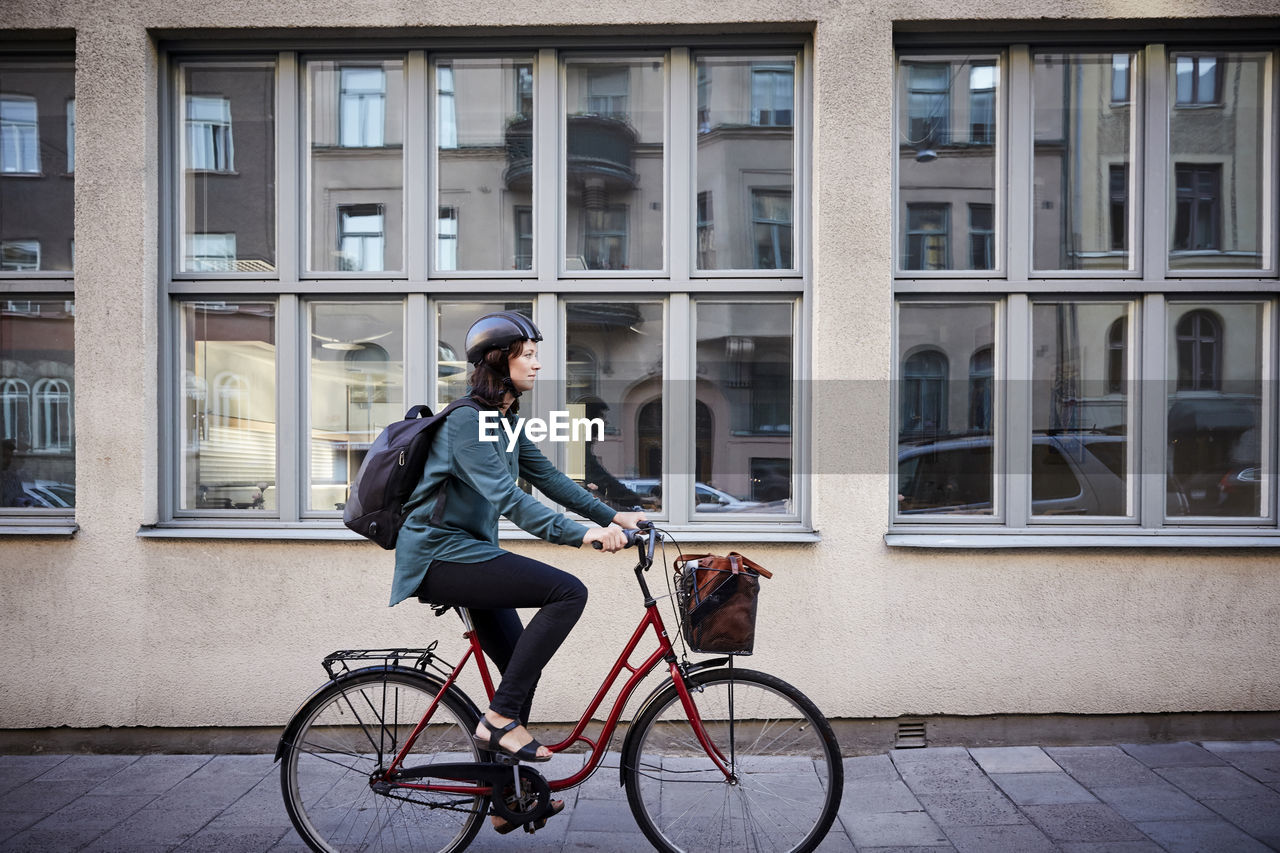 Side view of female engineer riding bicycle on street by building in city