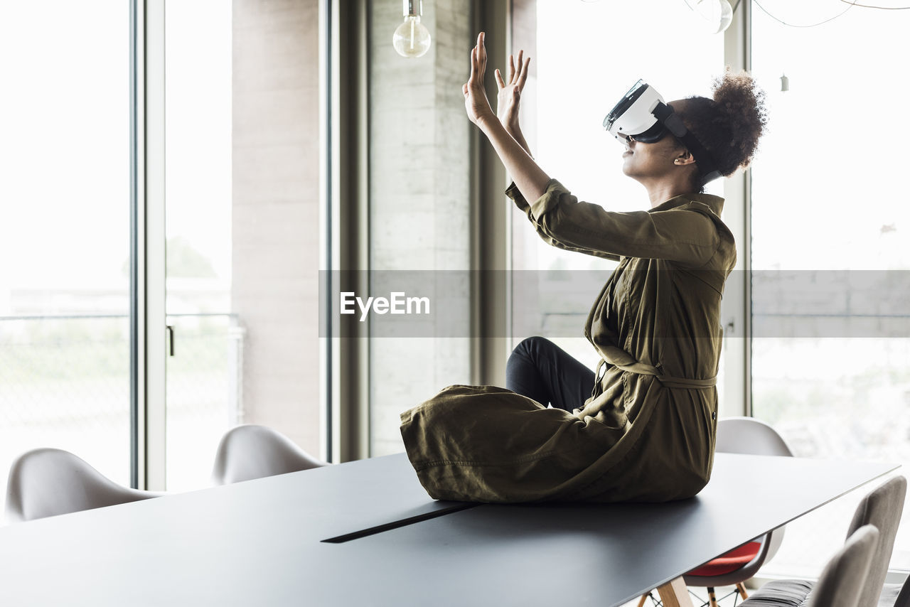 Woman in office sitting on conference table using virtual reality glasses