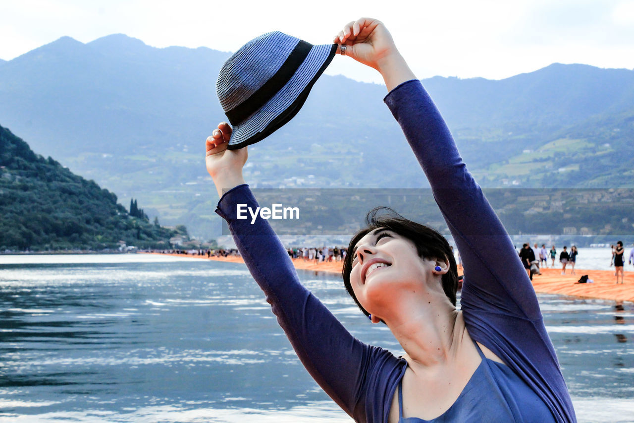 Young woman holding hat against mountains
