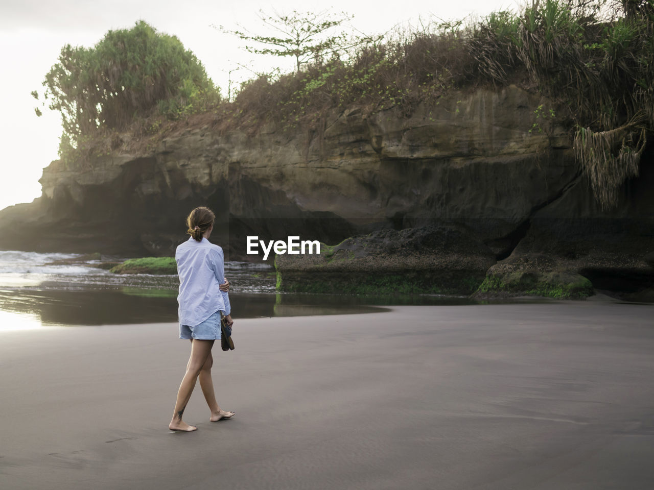 Young woman walking on a rocky beach, looking barefoot