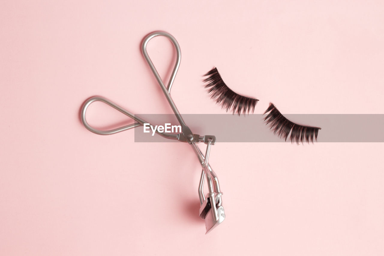 Flat lay composition of curler and false eyelashes on pink background, space for text