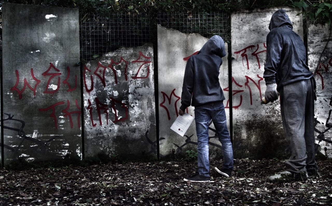 Rear view of men scribbling graffiti on metal gate