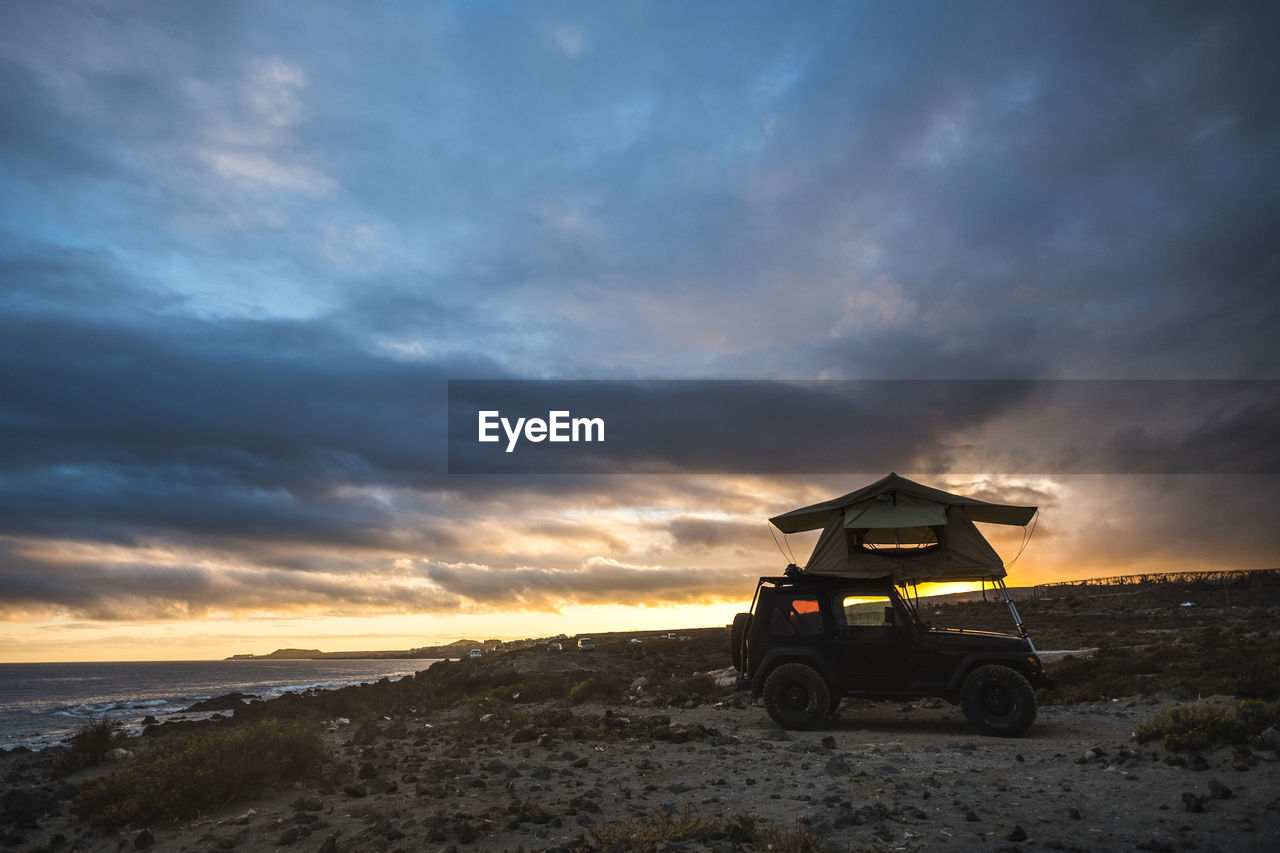 Tent on vehicle at beach against cloudy sky