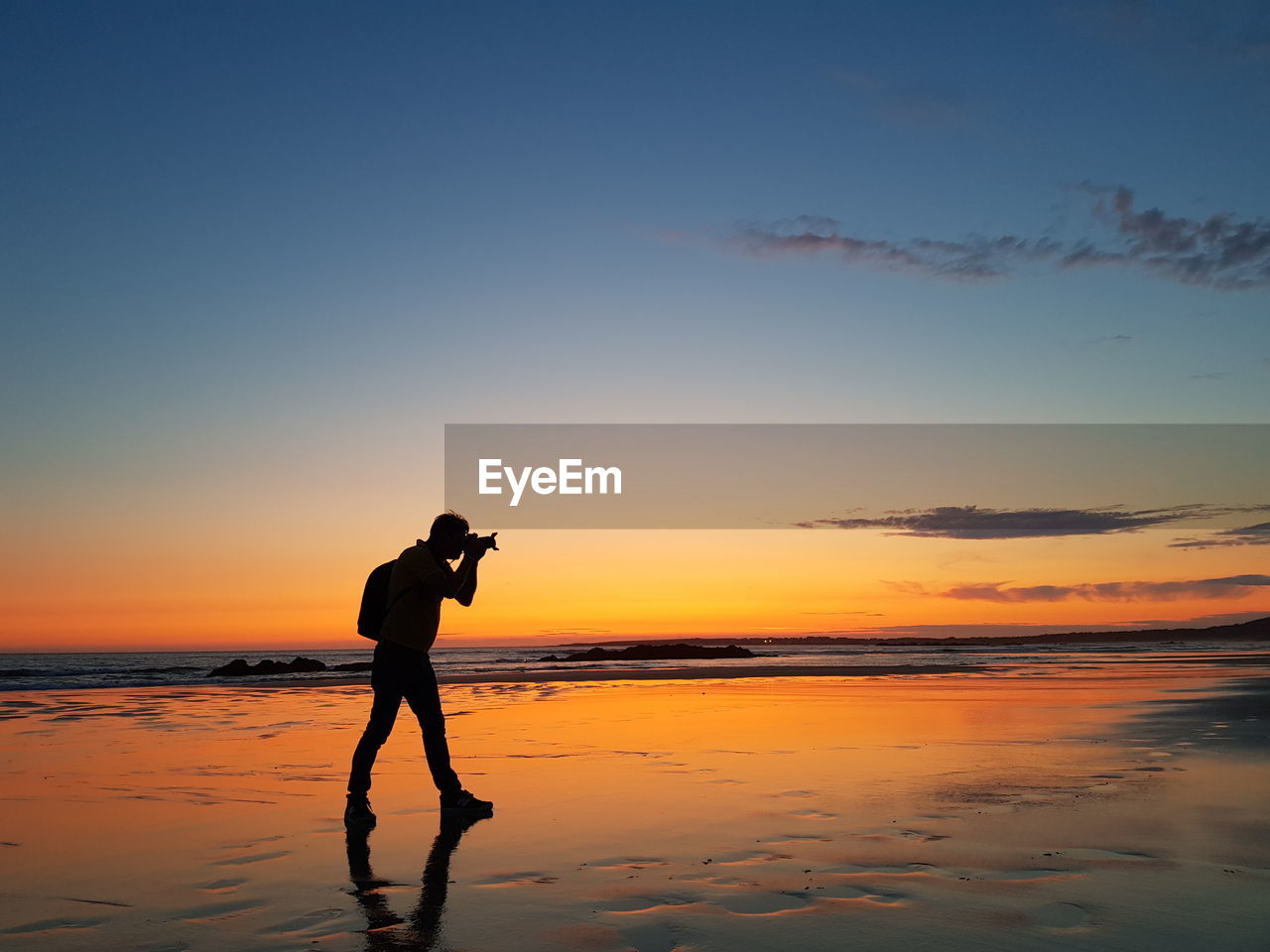 Silhouette man photographing at beach against sky during sunset