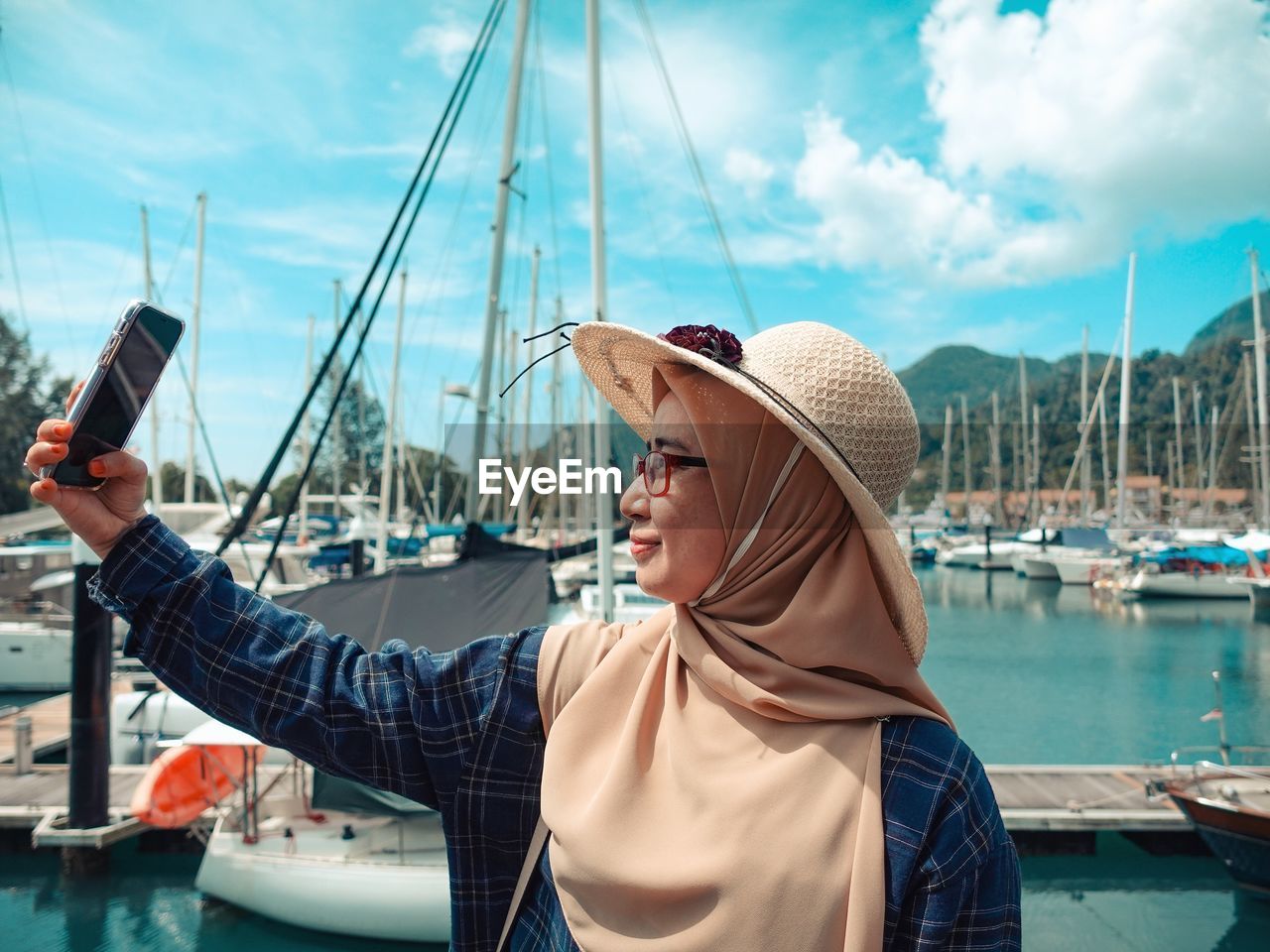 Woman wearing hijab taking selfie at harbor