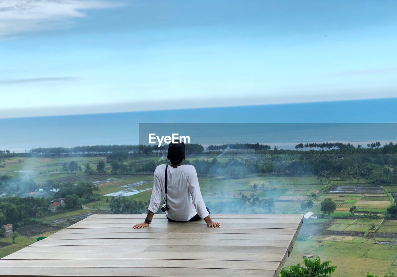 Rear view of man sitting on observation point against sky