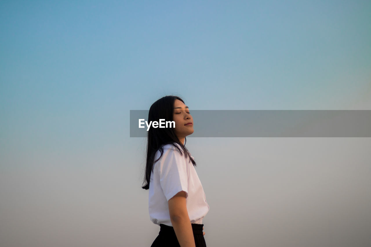 Young woman with eyes closed standing against sky during sunset
