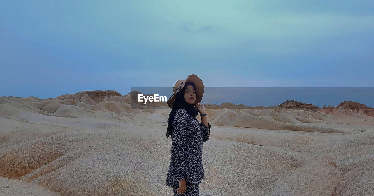 Portrait of young woman standing on desert against sky