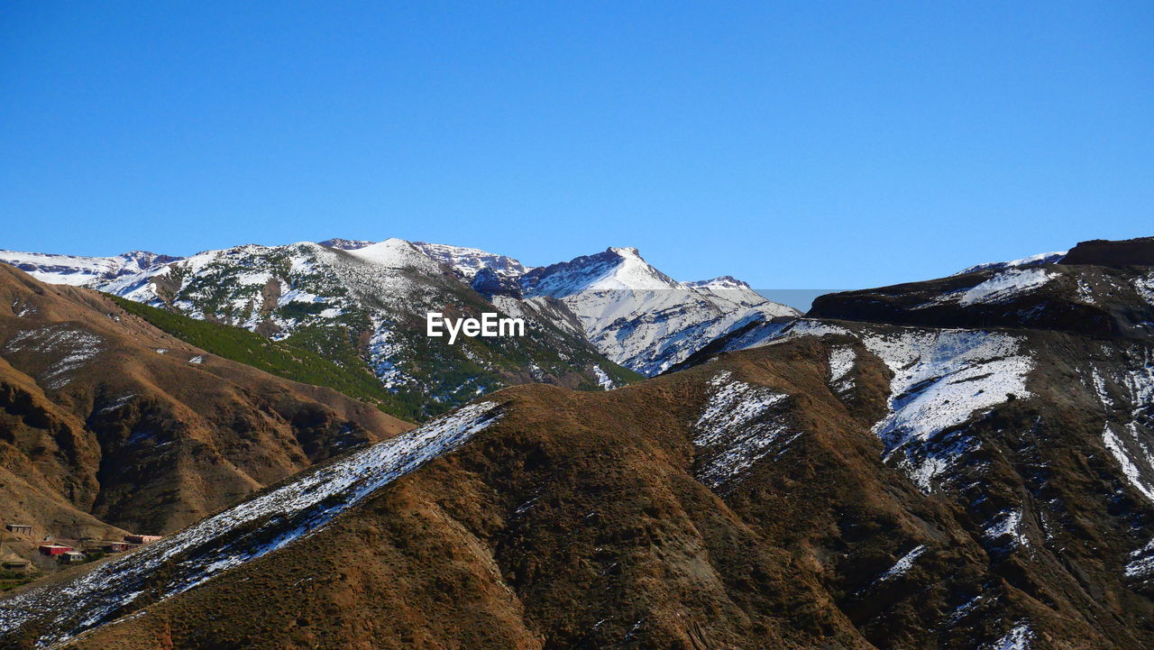 Low angle view of snowcapped mountains against clear blue sky