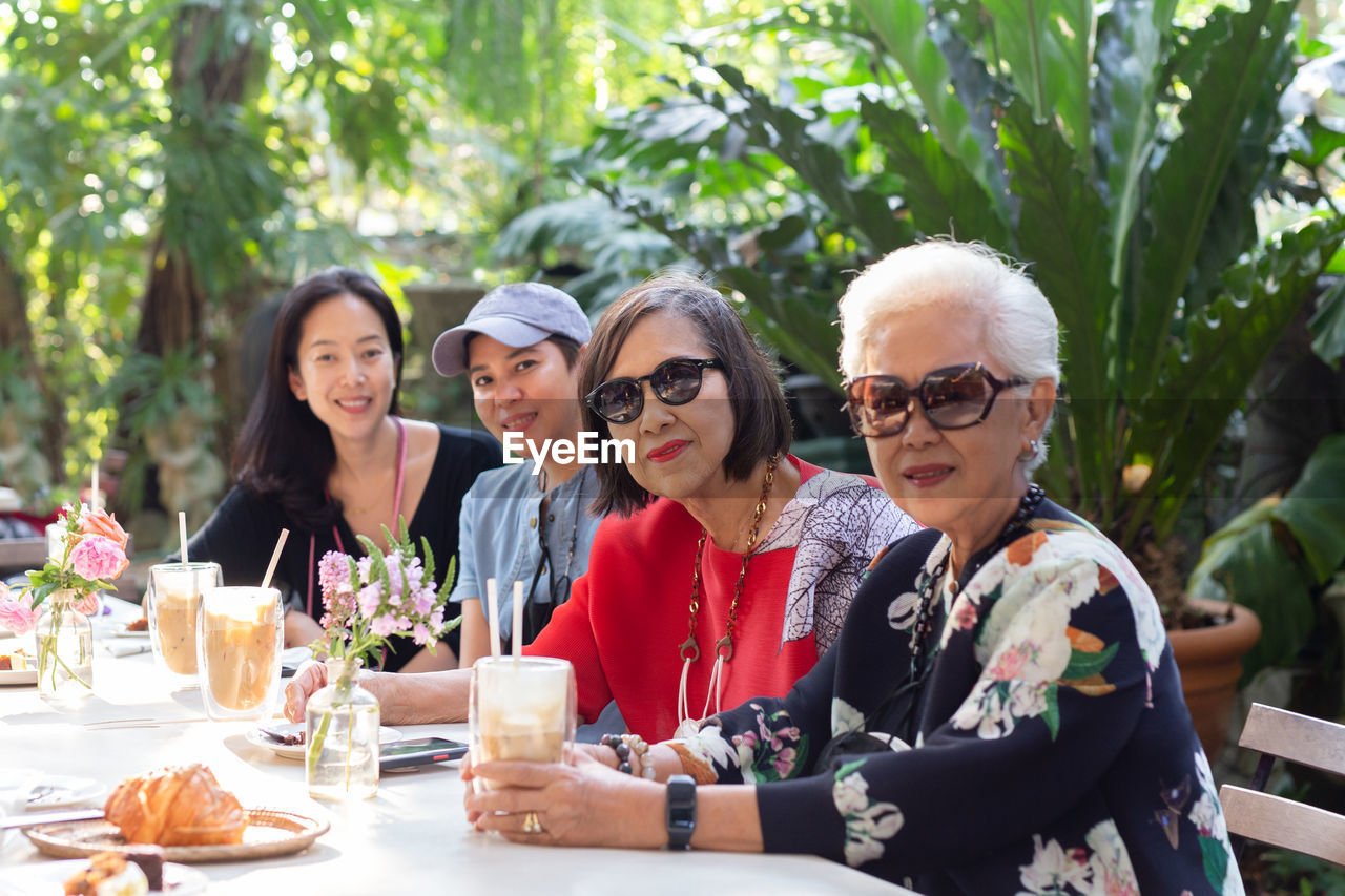 Asian senior woman and adult daughter drinking coffee at cafe outdoor.