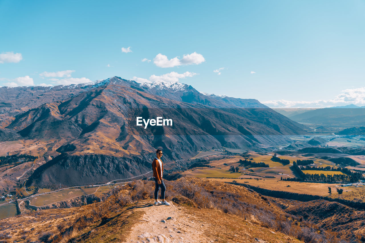 PERSON STANDING ON MOUNTAIN AGAINST SKY