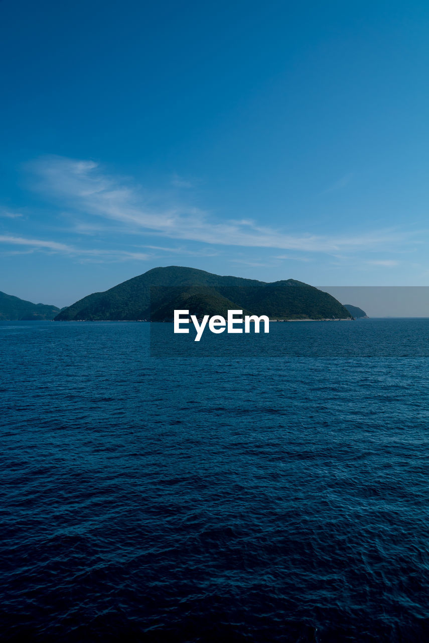 SCENIC VIEW OF SEA BY MOUNTAINS AGAINST BLUE SKY