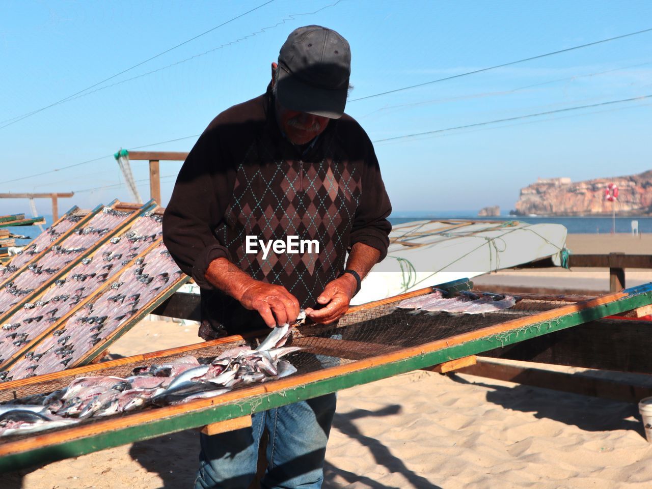 one person, adult, men, occupation, sky, nature, day, working, sunlight, standing, water, hat, nautical vessel, architecture, outdoors, roof, transportation, clothing, holding, casual clothing, clear sky