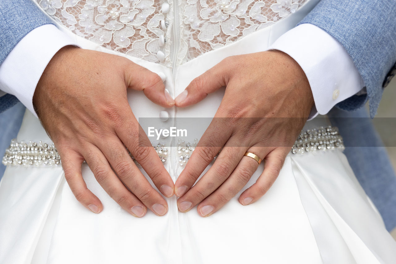 MIDSECTION OF WOMAN MAKING HEART SHAPE MADE FROM HANDS