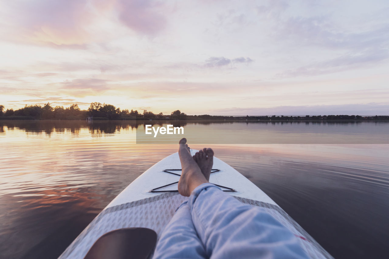 Legs of woman relaxing on paddleboard during sunset