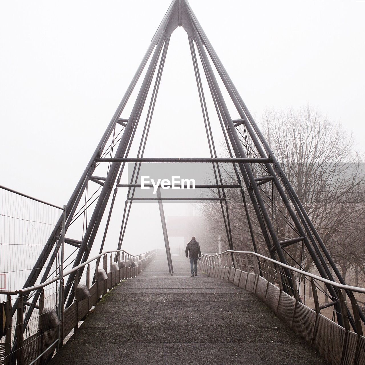 Rear view of man walking on footbridge during foggy weather