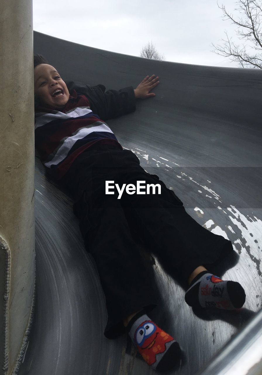 Low angle view of cheerful boy sliding on slide