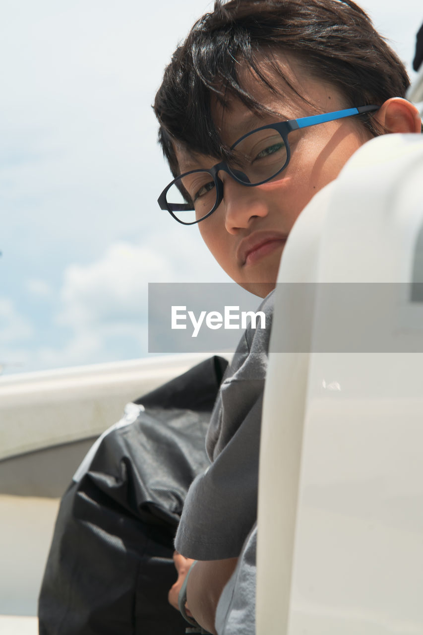 Asian boy wearing glasses looking at the camera on a boat.