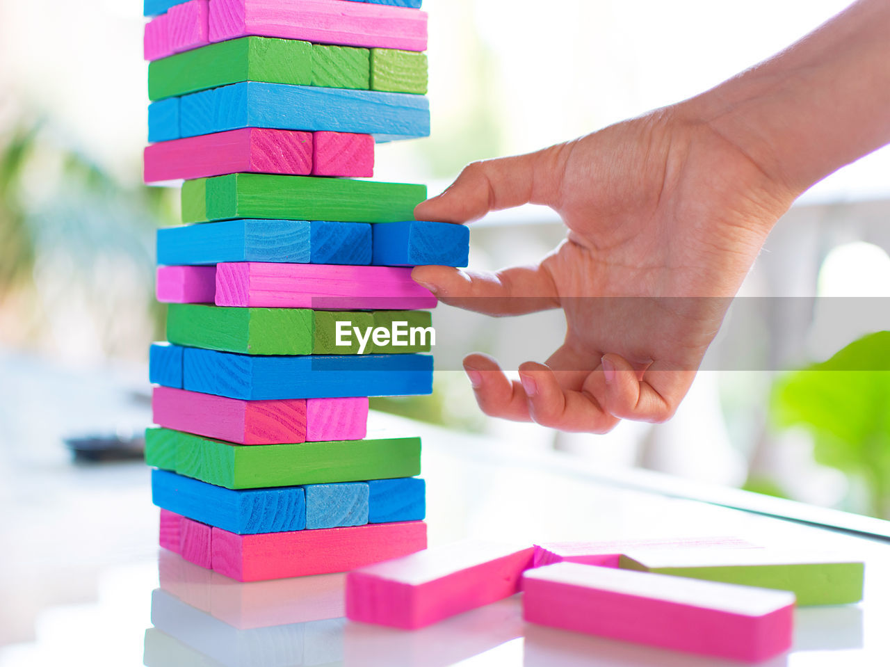 CLOSE-UP OF HAND HOLDING MULTI COLORED WOODEN STACK