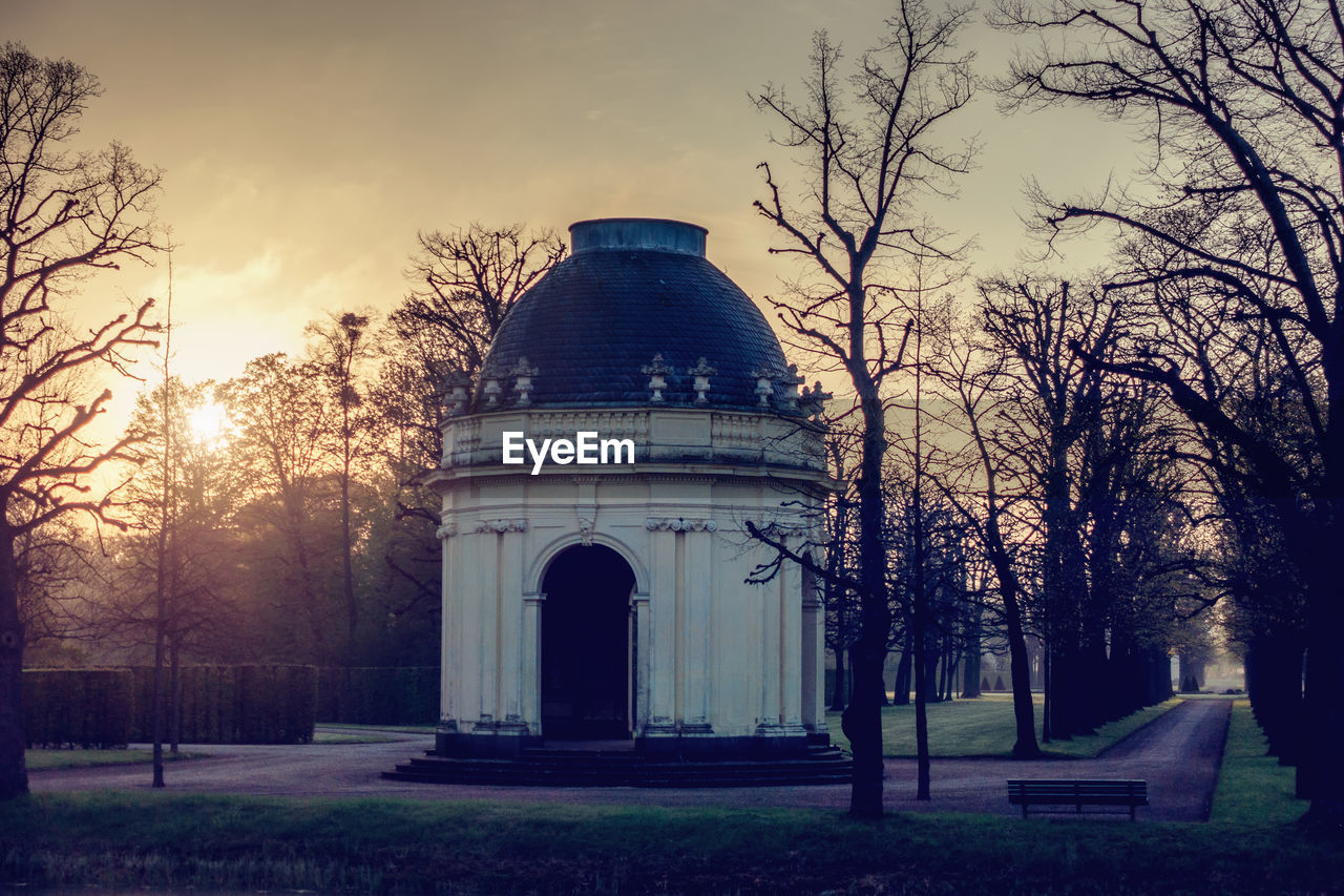 Built structure by bare trees against sky