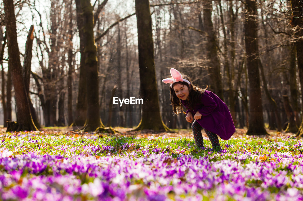 Woman with pink flowers on field by trees in forest