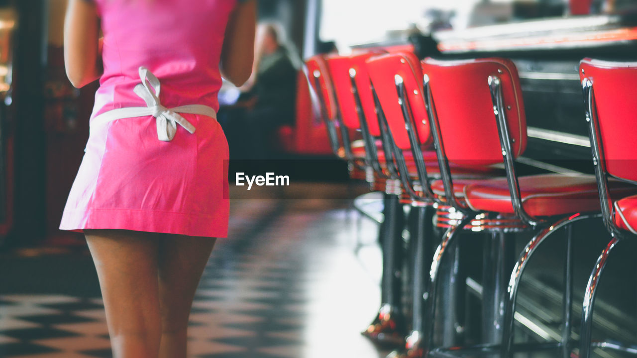 Midsection of waitress walking by chairs at restaurant