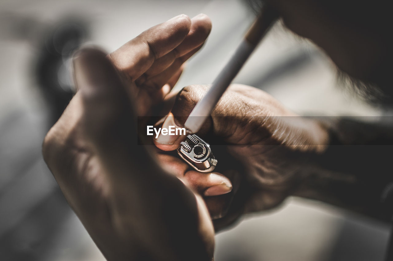 Cropped hand of man igniting cigarette outdoors