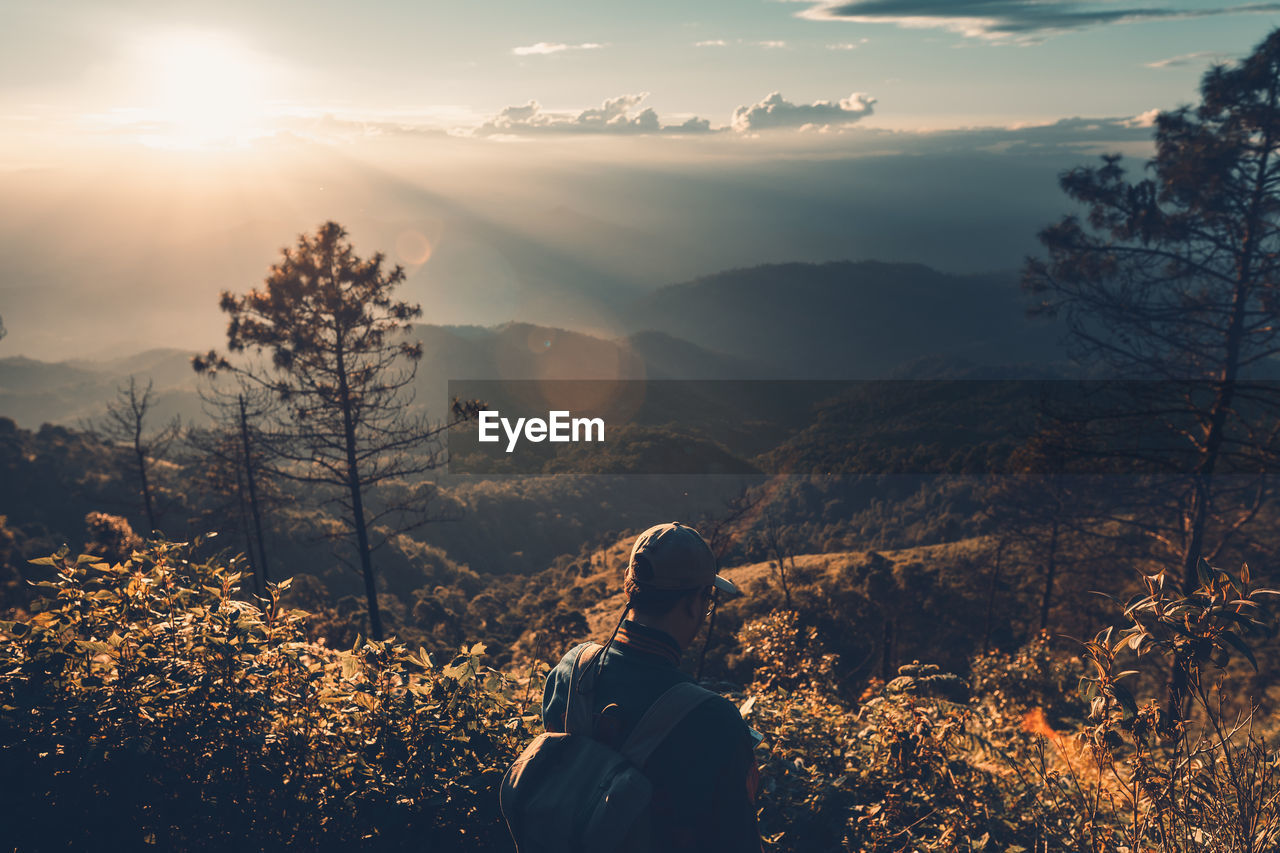 Rear view of man standing against mountains during sunset