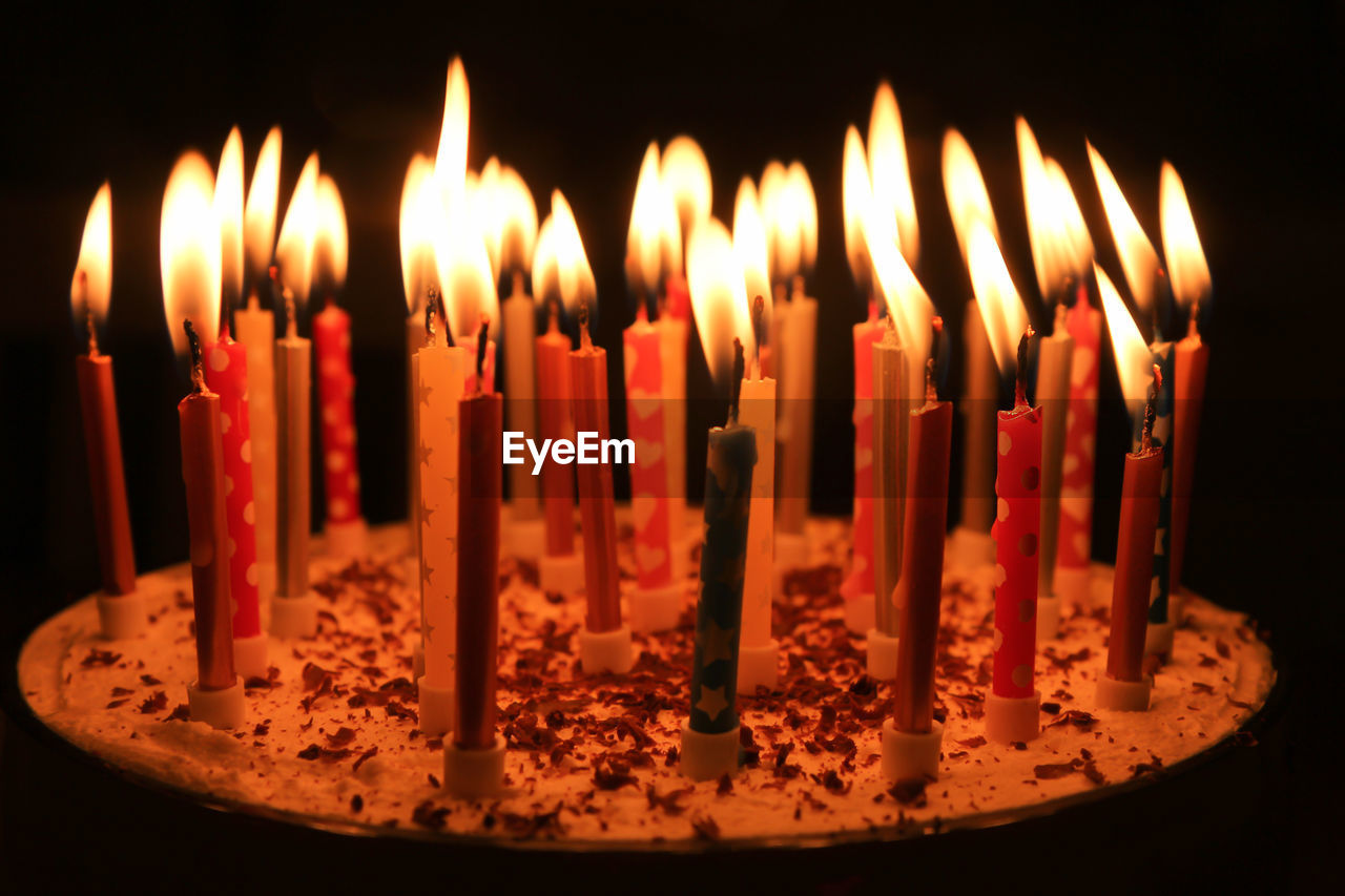Close-up of many candles on birthday cake in dark