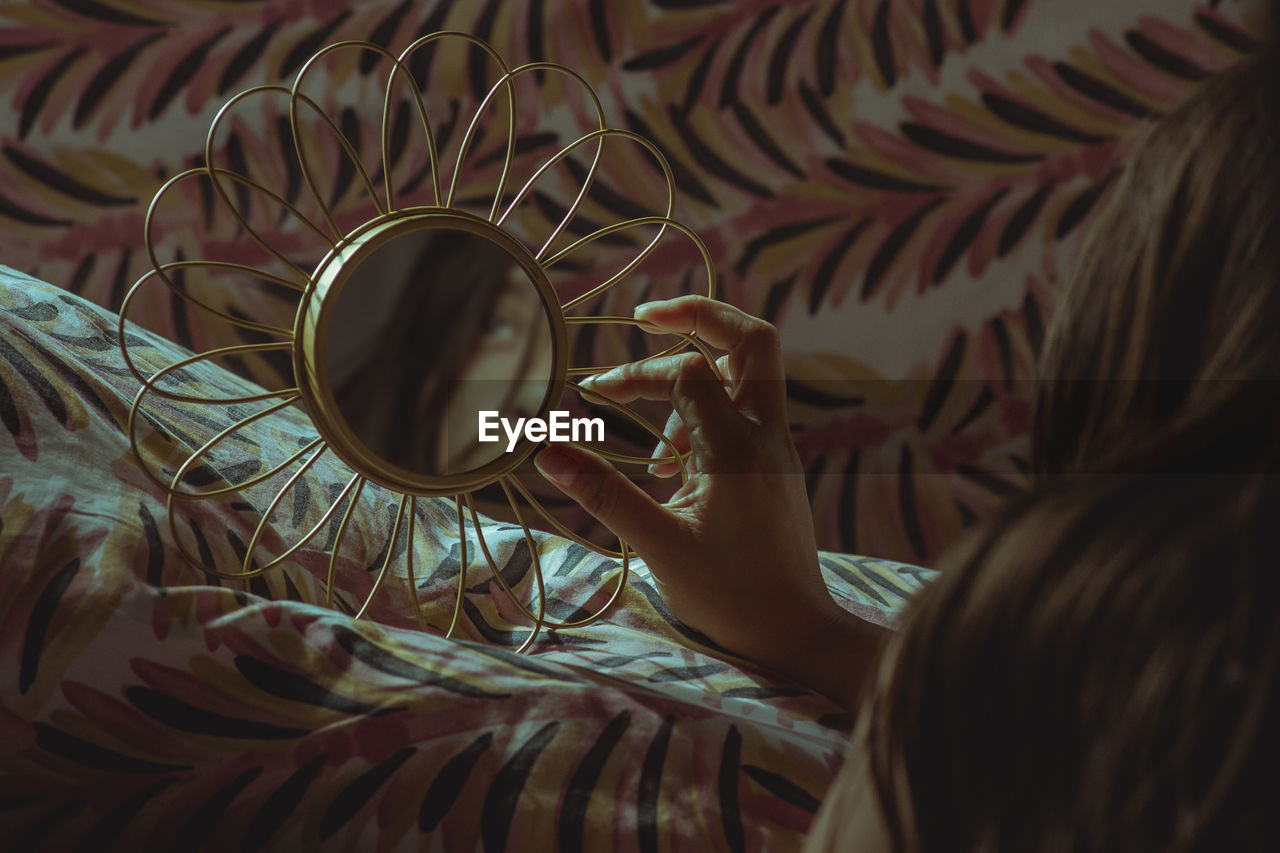 Close-up of woman holding mirror lying on bed