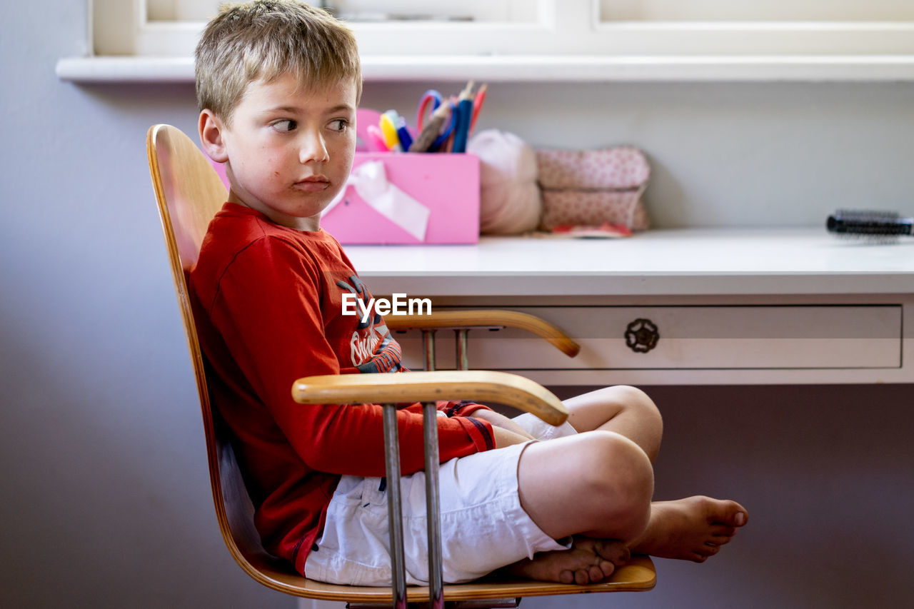 Side view of cute boy sitting on chair at home