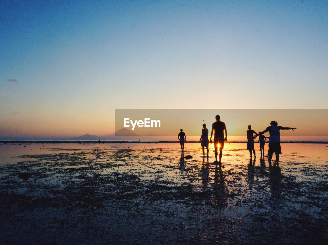 People enjoying on beach against sky during sunset