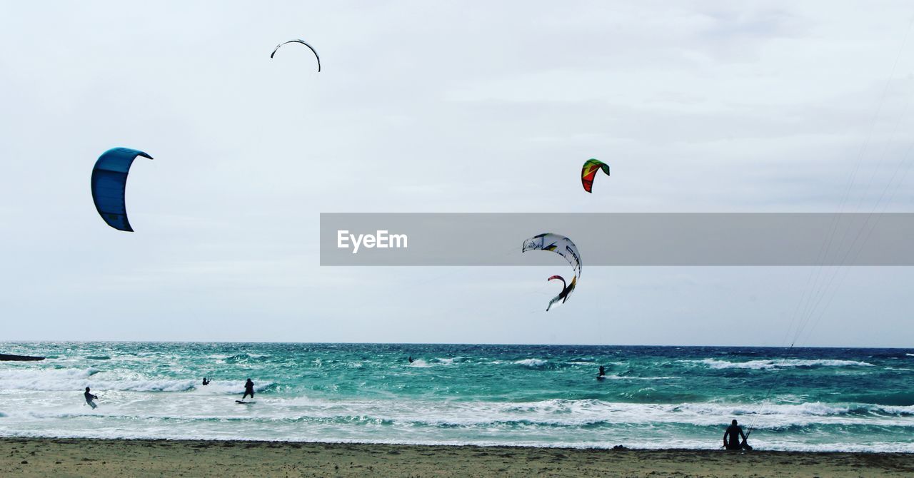 PEOPLE PARAGLIDING AT BEACH AGAINST SKY