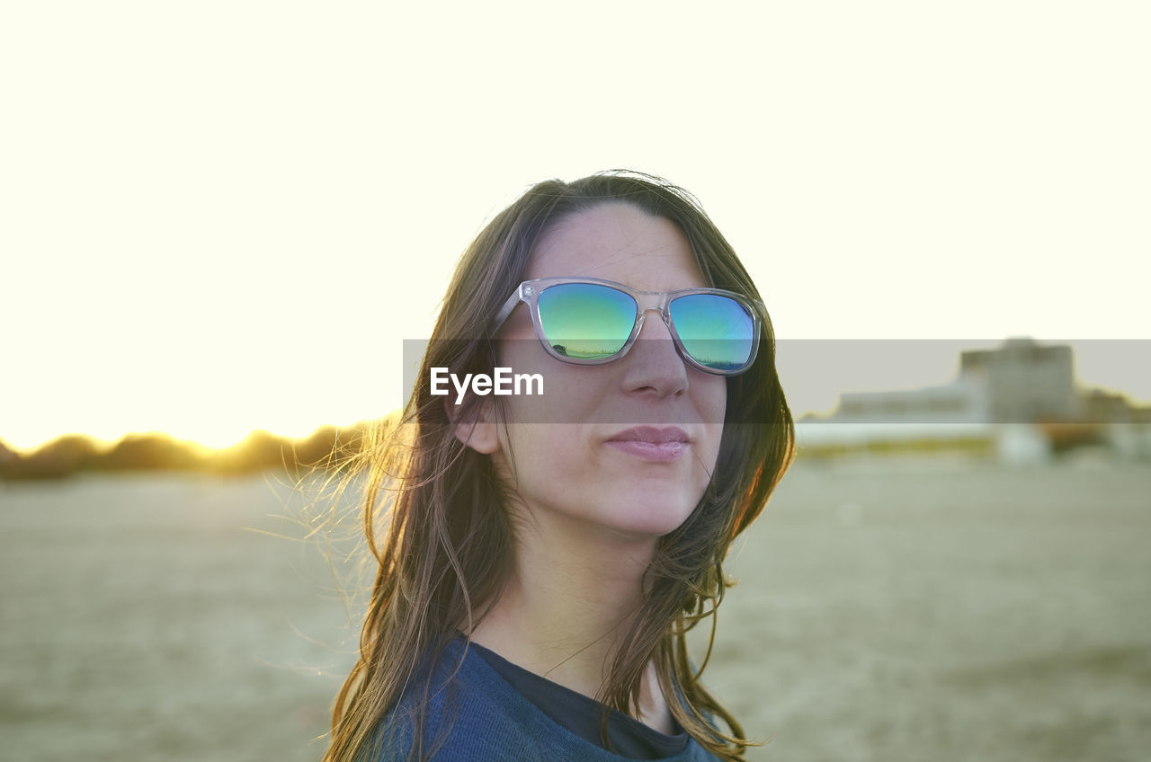 Close-up of young woman wearing sunglasses at beach against sky during sunset