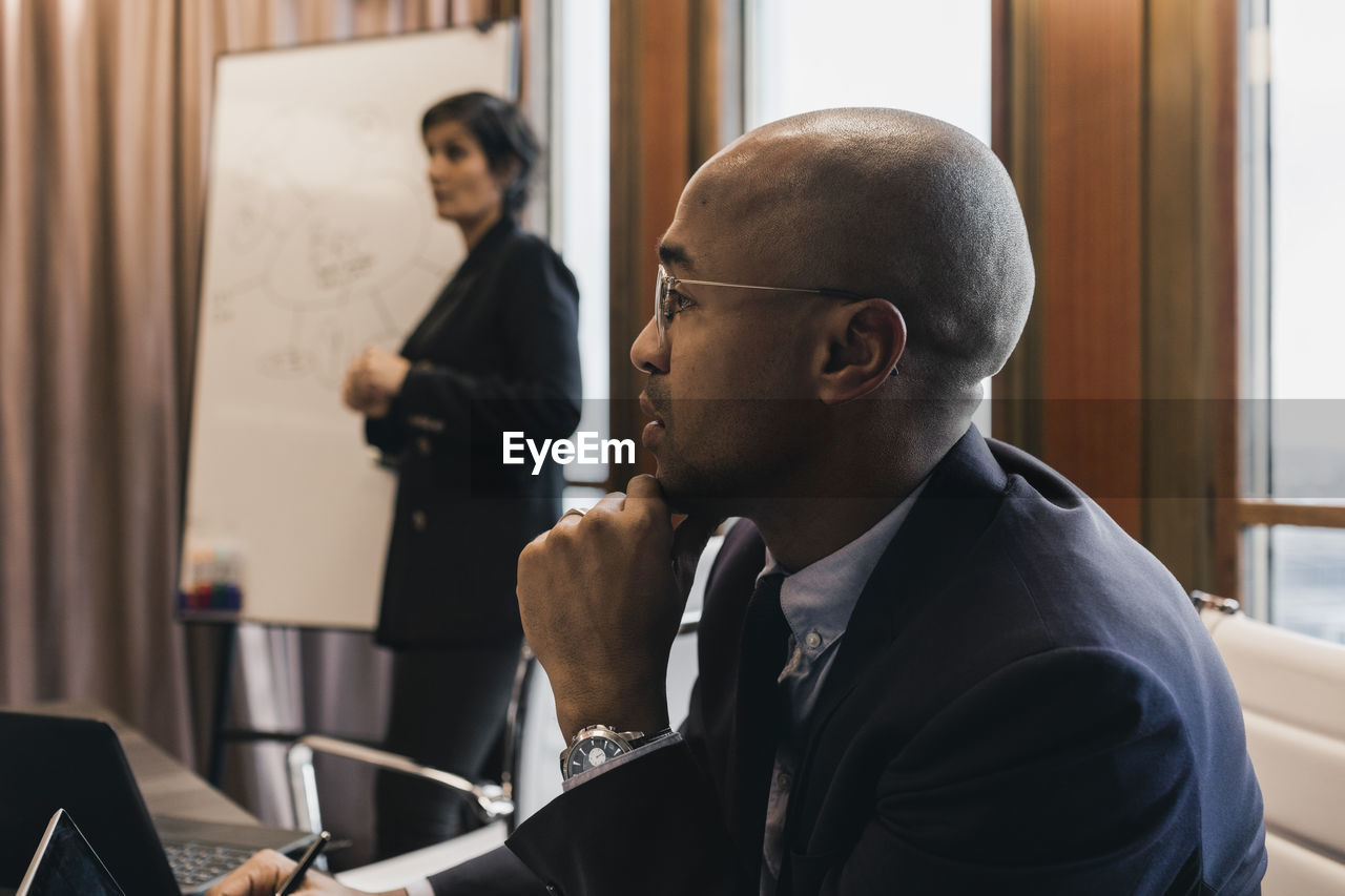 Bald businessman with hand on chin with female colleague in board room during meeting